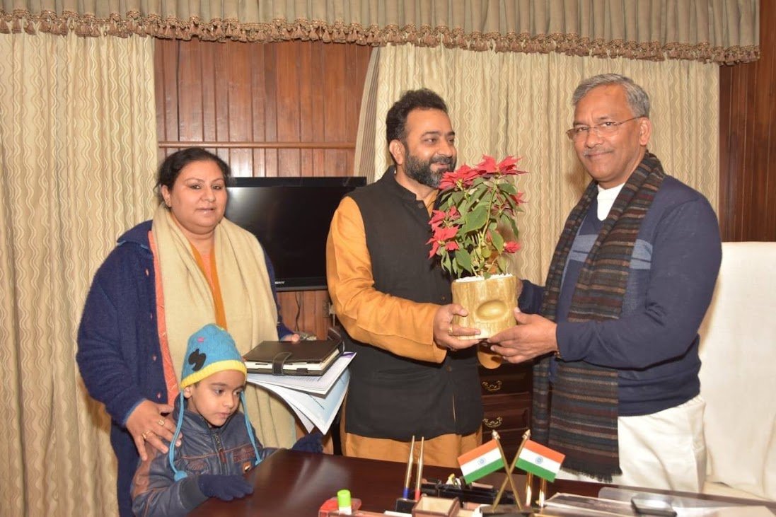 Dhananjay's family presenting a potted plant to a dignitary at an official meeting, the Indian tricolour on the desk